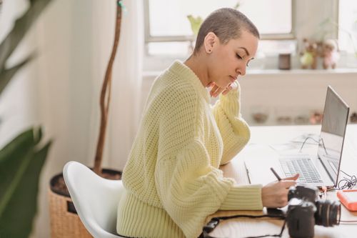 Free Side view of serious female with short hair drawing with stylus while editing photos at table with photo camera during work in room with green plant Stock Photo