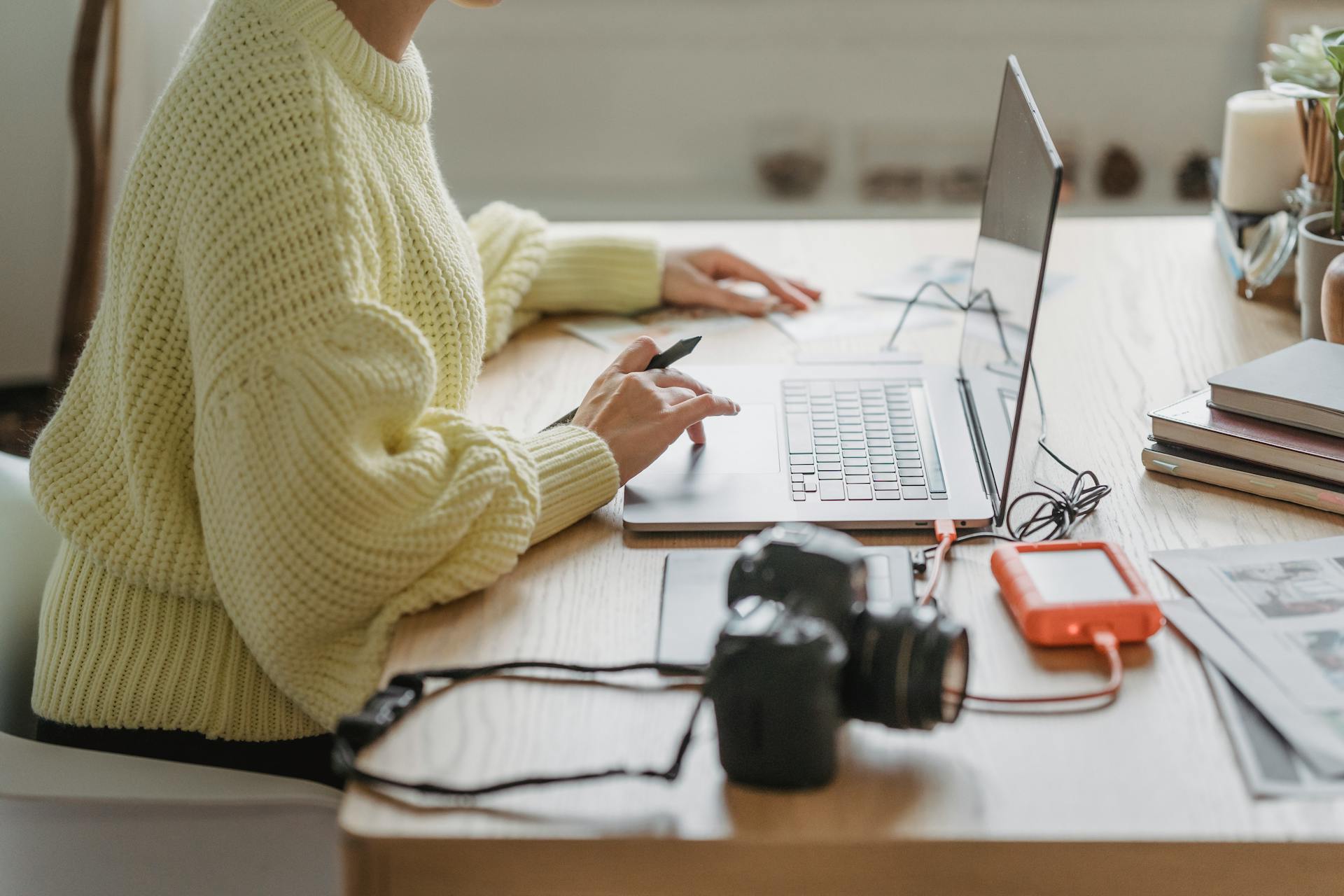 Unrecognizable woman uses a laptop and editing tools in a cozy workspace.