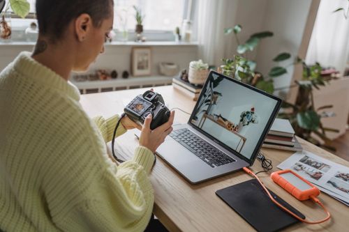 Free Side view of crop concentrated female photographer looking at screen of photo camera while sitting at table with netbook and graphic tablet Stock Photo