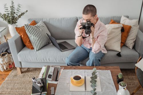 Free Unrecognizable concentrated female photographer with short hair taking picture of photography composition with cup of tea and green branch on table Stock Photo