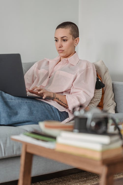 Free Concentrated young female in casual clothes browsing modern netbook and lying on comfy couch in light living room Stock Photo