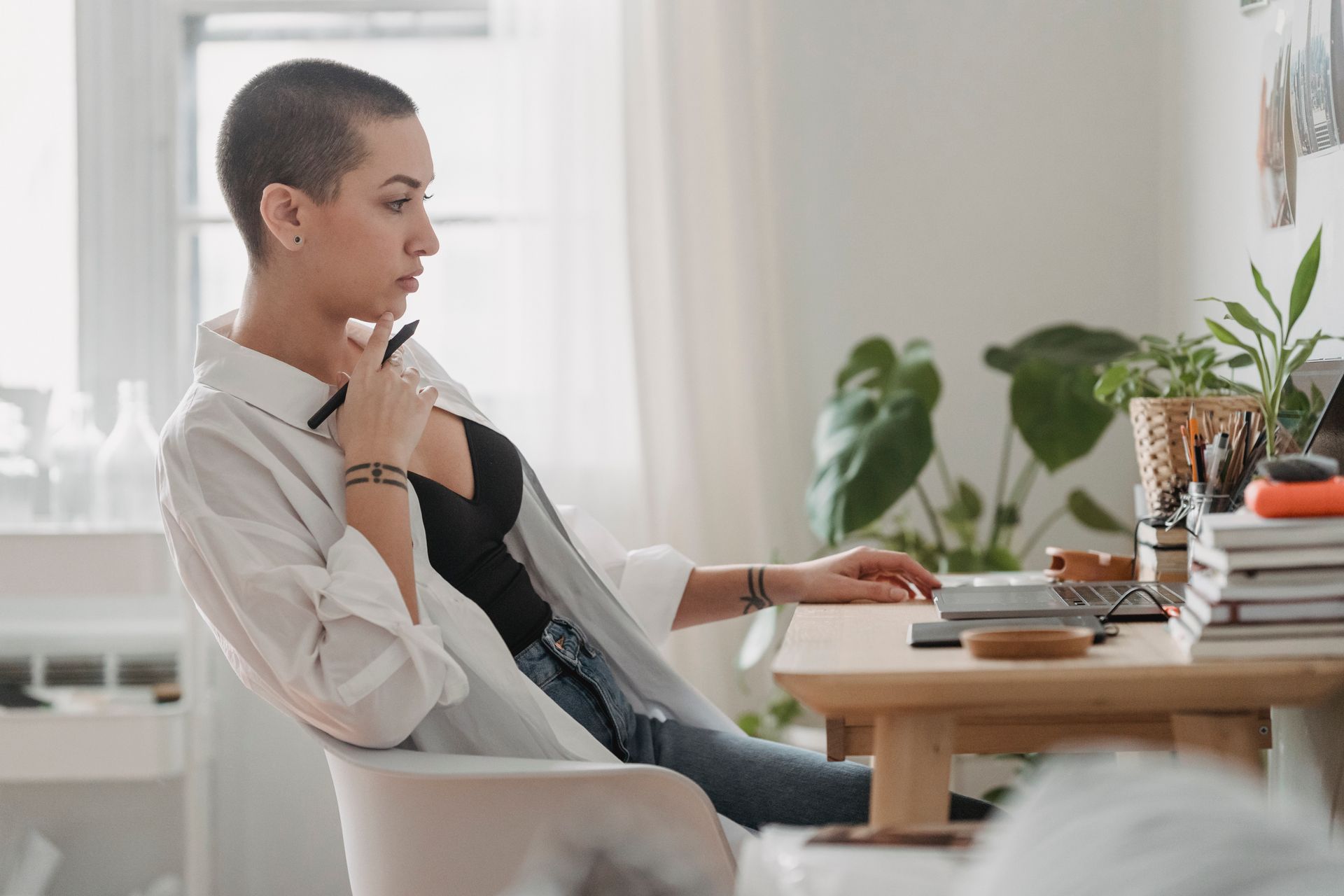 Young woman with short hair working thoughtfully at home office desk, using laptop.