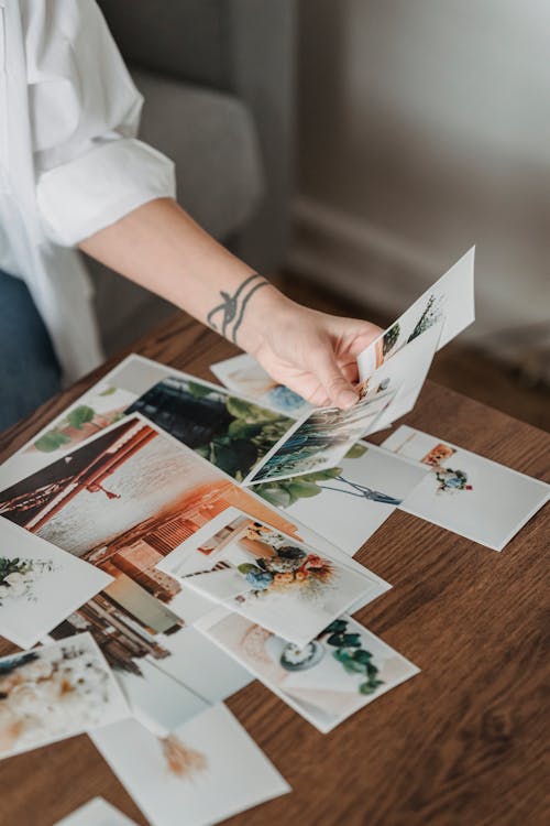 Free High angle anonymous female looking through printed pictures scattered on table in light room Stock Photo