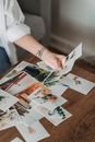 High angle anonymous female looking through printed pictures scattered on table in light room
