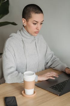 A young woman in casual attire focuses intently on her laptop while working from home.
