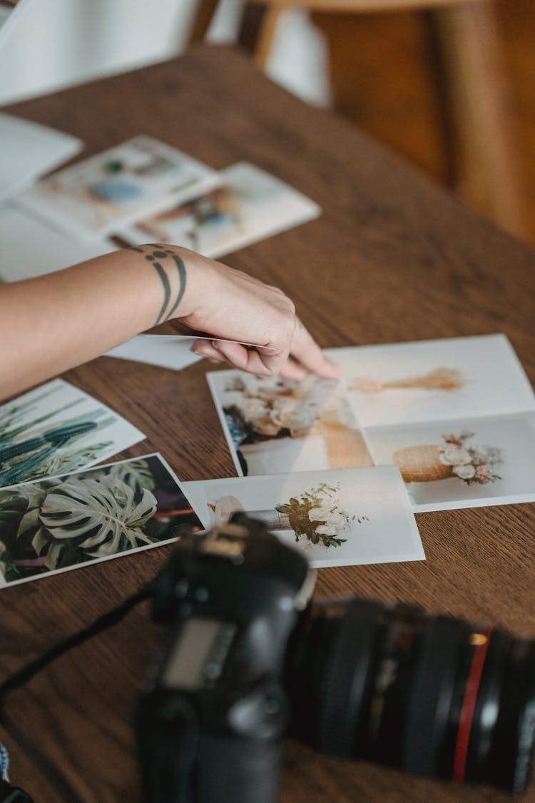 Crop Anonymous Person Pointing At Photos Scattered On Table