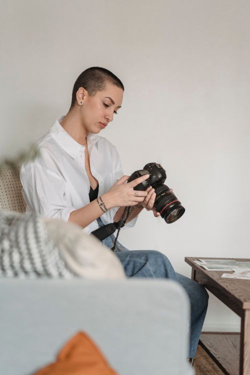 Free Pensive female photographer in casual wear setting professional photo camera and sitting on comfy couch in living room Stock Photo