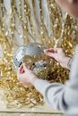 Crop faceless person decorative disco ball against golden tinsels