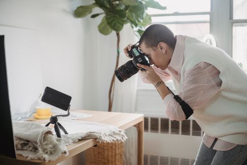 Free Side view focused female photographer in casual wear taking photo on modern photo camera of smartphone tripod placed on table in light studio Stock Photo