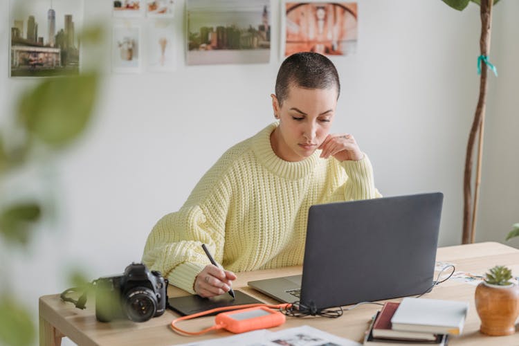 Contemplative Woman Drawing On Graphic Tablet And Working On Laptop