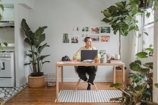 Modern workspace featuring a laptop, indoor plants, and a thoughtful individual in a bright home office.