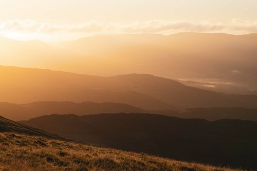 Free Peaceful view of rolling hills and mountains bathed in warm golden hour light. Stock Photo