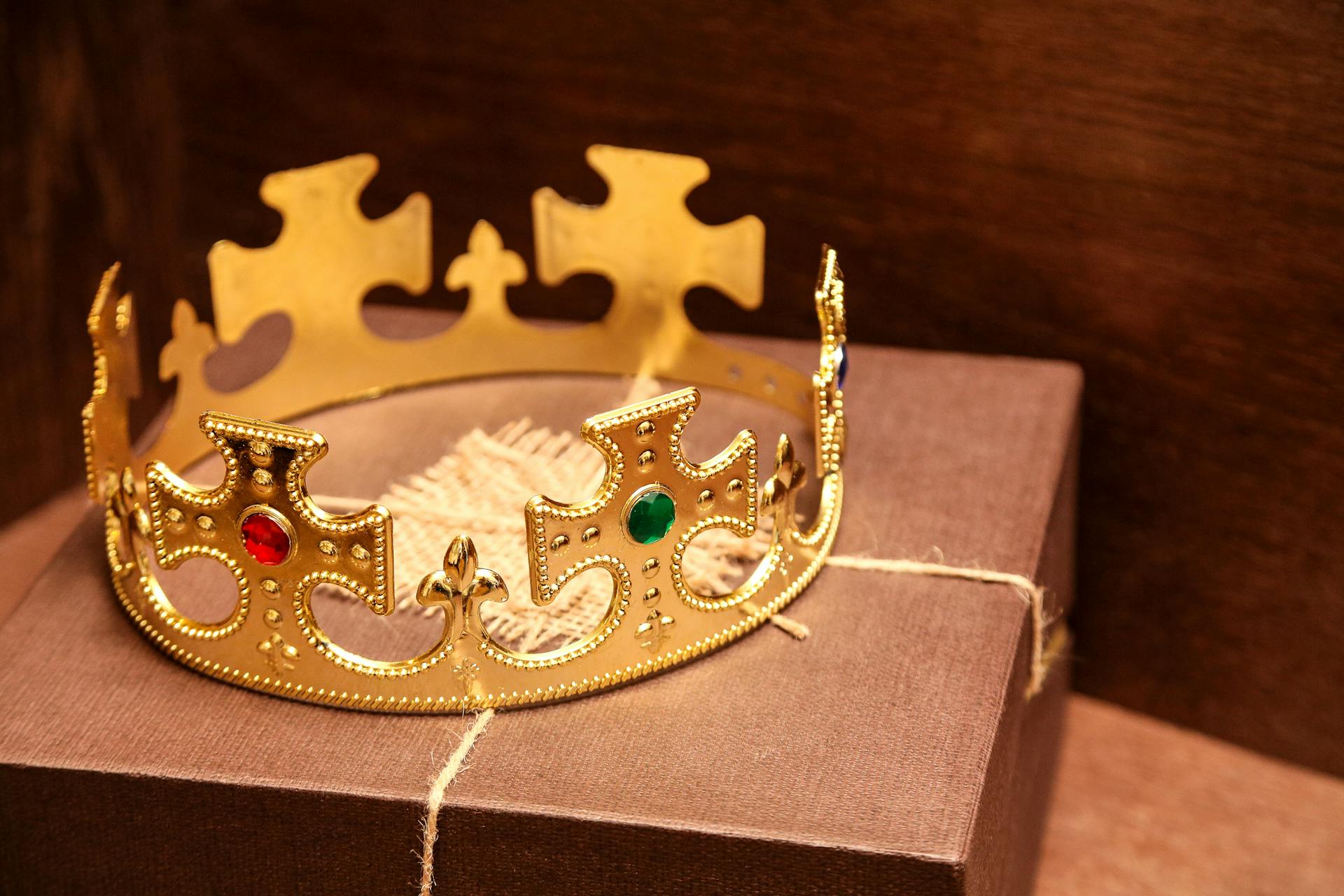 A luxurious gold crown with gems sits atop a brown gift box in a rustic setting.