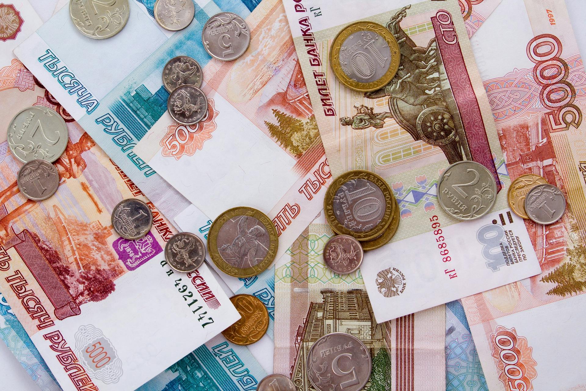 A detailed image of Russian ruble banknotes with various coins scattered on top, showcasing currency details.