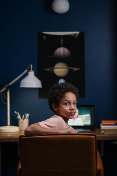 Young child engaged in online learning at home, seated at desk with laptop.