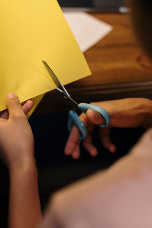 Free A person's hands skillfully cutting yellow paper with scissors on a wooden table. Stock Photo