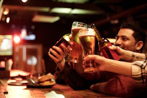Free Friends celebrating and toasting with beers in a warm and cozy bar environment for joy and friendship. Stock Photo