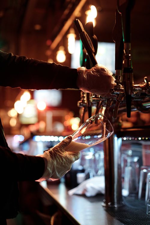 Free Bartender pours beer at a lively bar, creating a perfect evening ambiance. Stock Photo