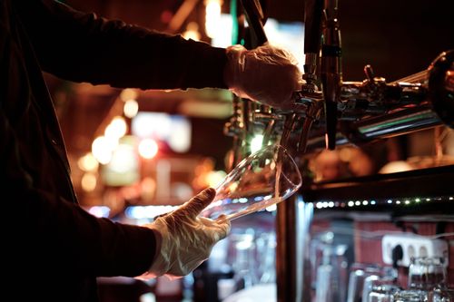 Free Bartender with gloves pouring beer into a glass in a dimly lit nightclub. Stock Photo