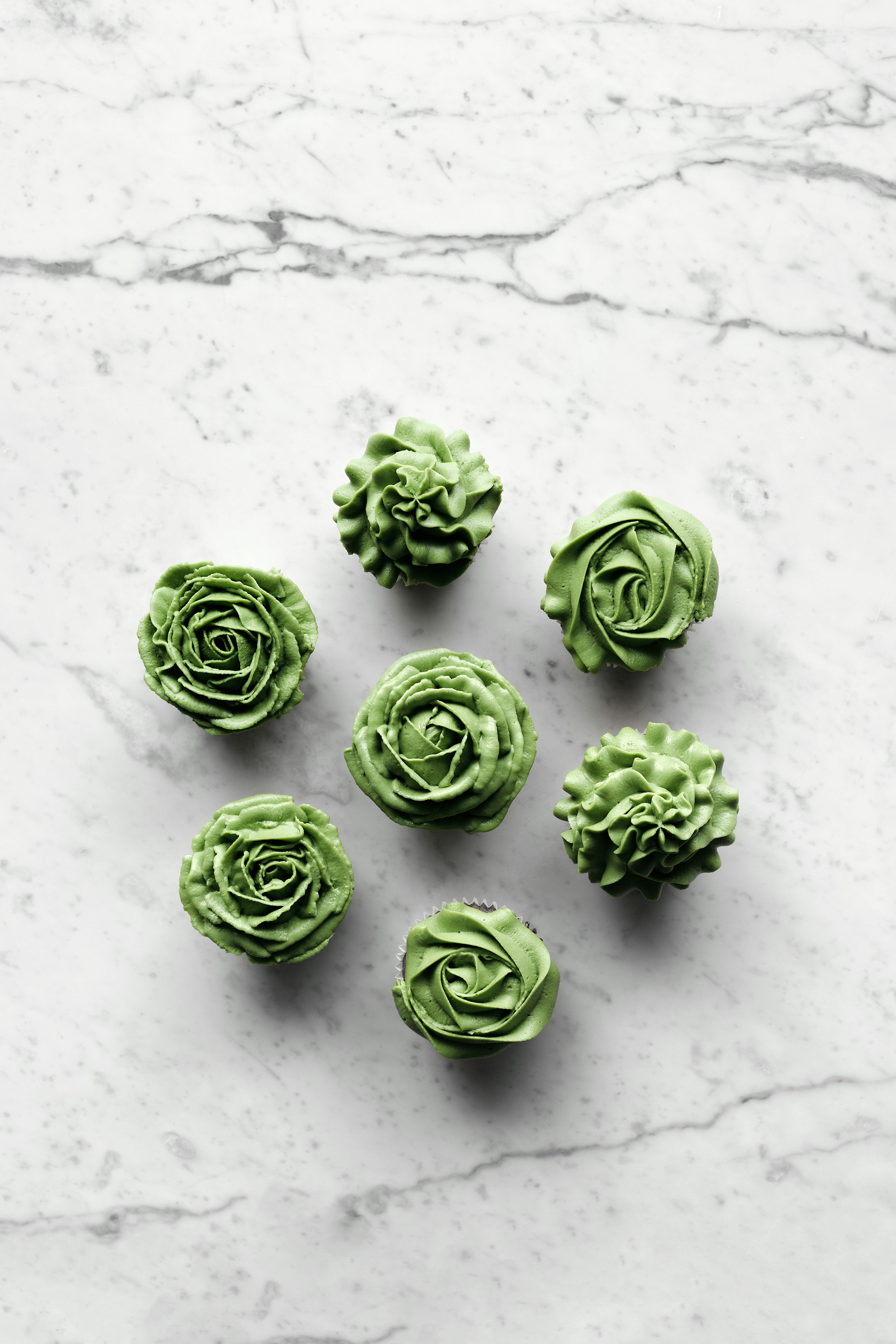 Top view of green rose-themed cupcakes arranged on a marble surface, perfect for elegant celebrations.