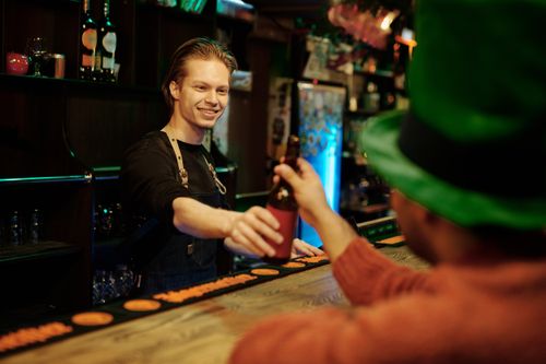 Free Bartender smiling and serving drinks to a customer in festive setting. Stock Photo
