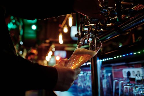 Free A person pours beer from a tap into a glass at a dimly lit bar, capturing a lively atmosphere. Stock Photo