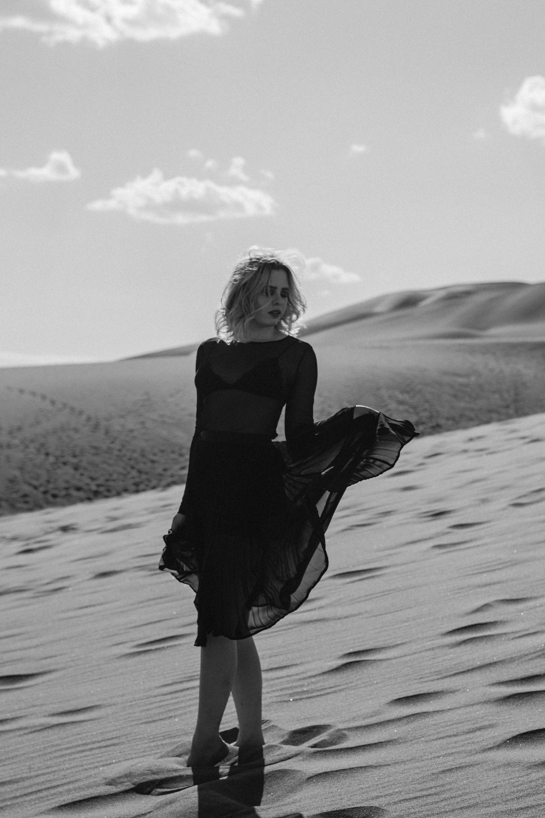 Black-and-white portrait of a woman in a flowing dress standing in a desert.