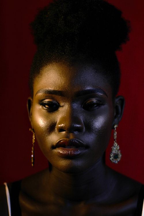Free Close-up portrait of a woman with afro hairstyle, wearing earrings, against a red background. Stock Photo