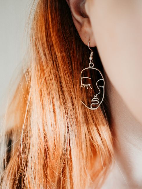 Close-up of a minimalist face line art earring worn by a woman with red hair.