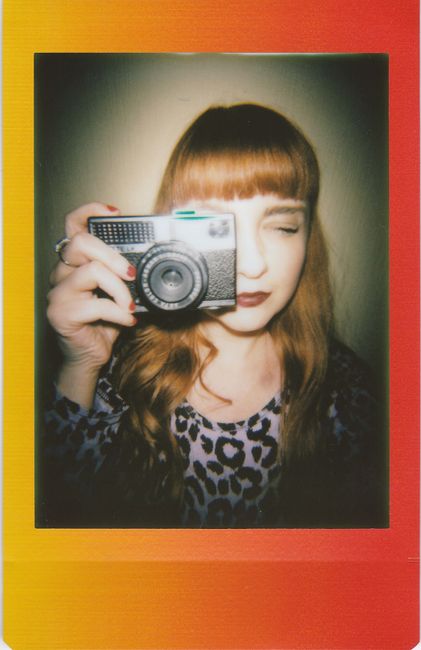 A woman with red hair holding a vintage camera, captured in a vibrant frame.