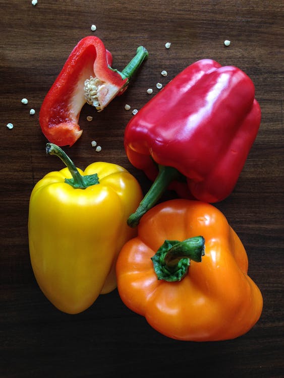 Three Yellow, Red and Orange Bell Peppers on Brown Surface