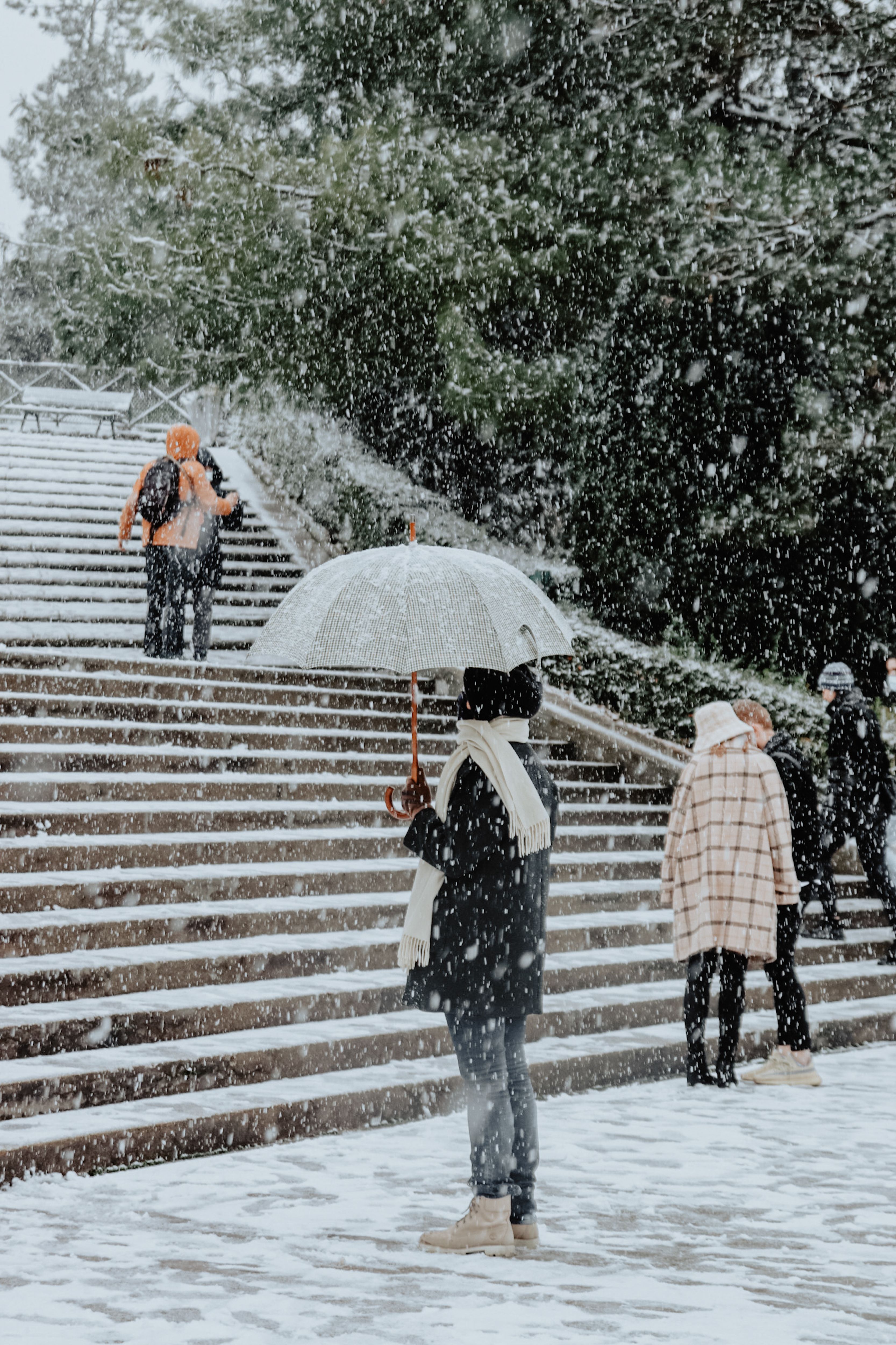 People walking in snow with umbrellas on a wintery outdoor staircase.