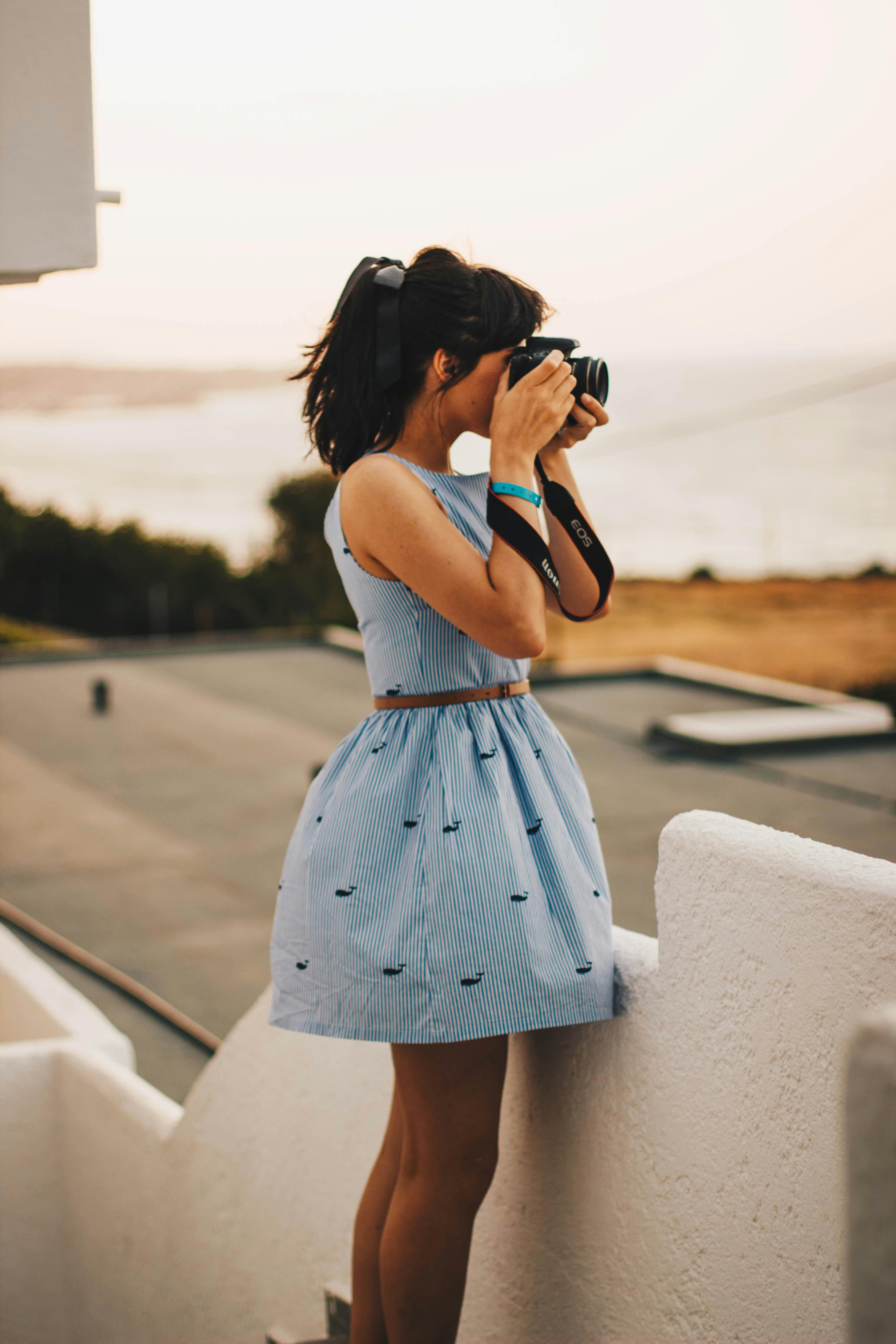 A young woman capturing outdoor scenery with a camera in a serene, sunny location.