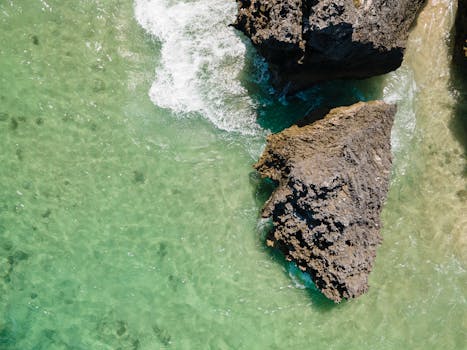 A top-down view of rocks on a sandy shoreline with clear waves.