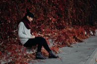 一名女子若有所思地坐在路边，周围是鲜艳的秋叶