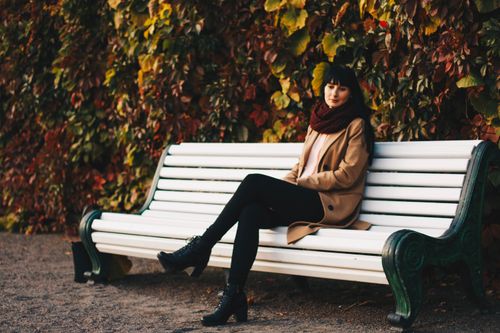 Free Woman in stylish autumn outfit sitting on a park bench with colorful leaves. Stock Photo