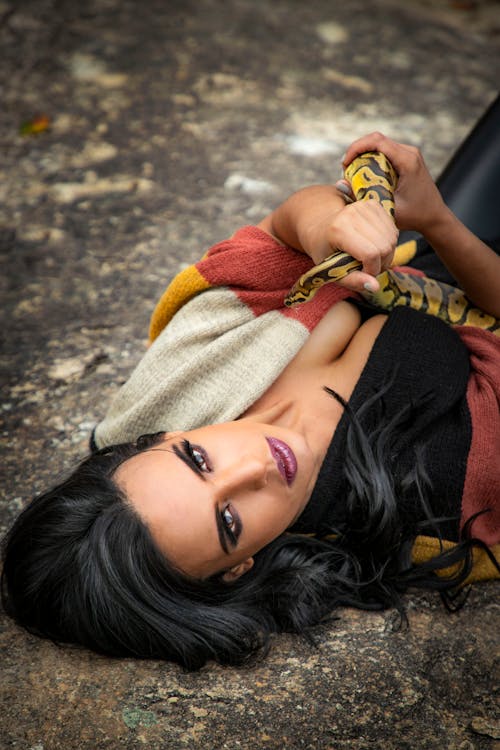 Woman Lying on the Ground while Holding a Snake