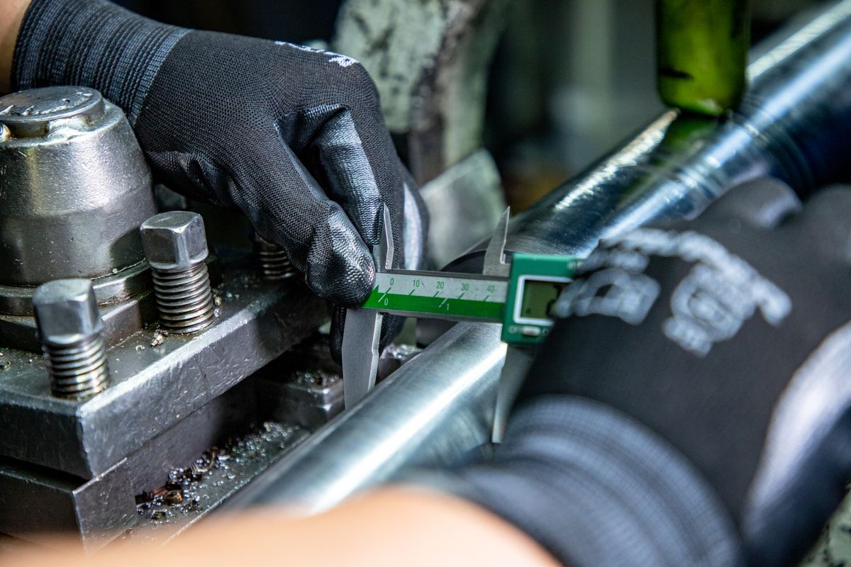 A close-up of a person using a caliper to measure a machined metal part, emphasizing precision metrology