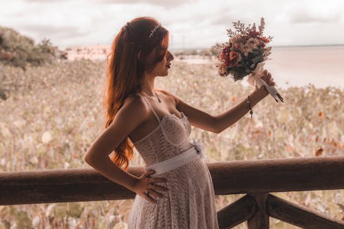 Pregnant Woman in White Lace Strap Dress Holding Bouquet of Flowers