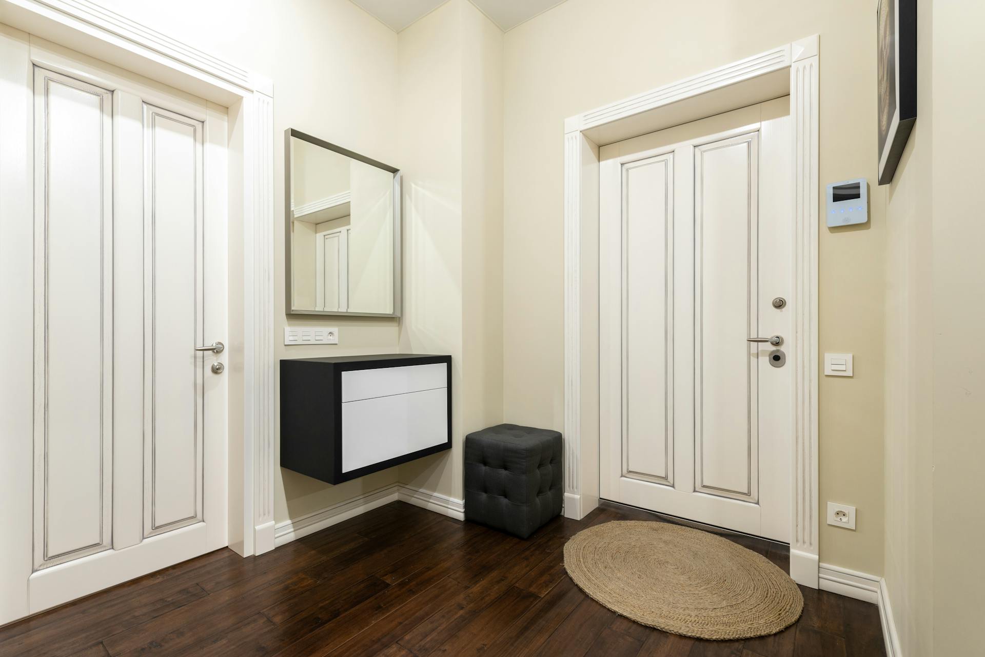 Contemporary corridor interior with carpet and pouf on parquet under cabinet and mirror between doors at home