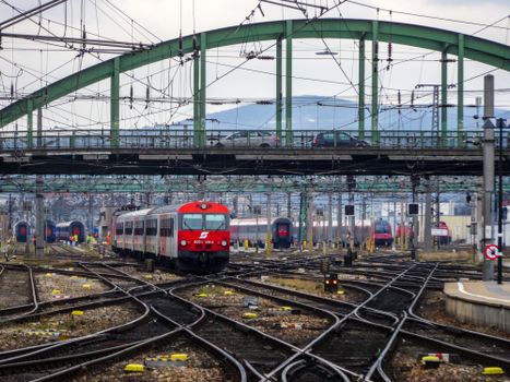 A busy railway scene in Vienna with multiple trains and tracks under a large bridge.