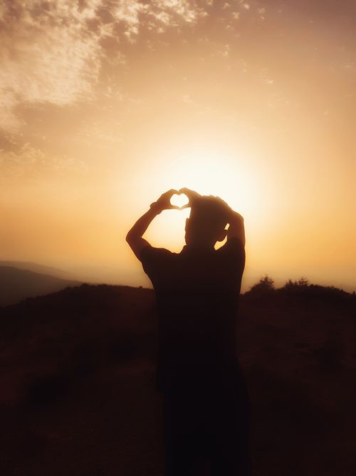 Free Silhouette of a person forming a heart shape with hands against a stunning sunset in Mouzaia, Algeria. Stock Photo