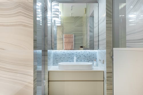 Creative design of bathroom with washbasin between cabinet and mirror reflecting bright lamps and towels in house