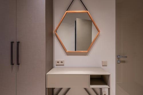 Hexagonal shaped mirror hanging on wall above cabinet and switch between closet and door in modern house