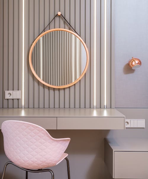 Stylish empty vanity table under round mirror on wall near light pink armchair in stylish bedroom