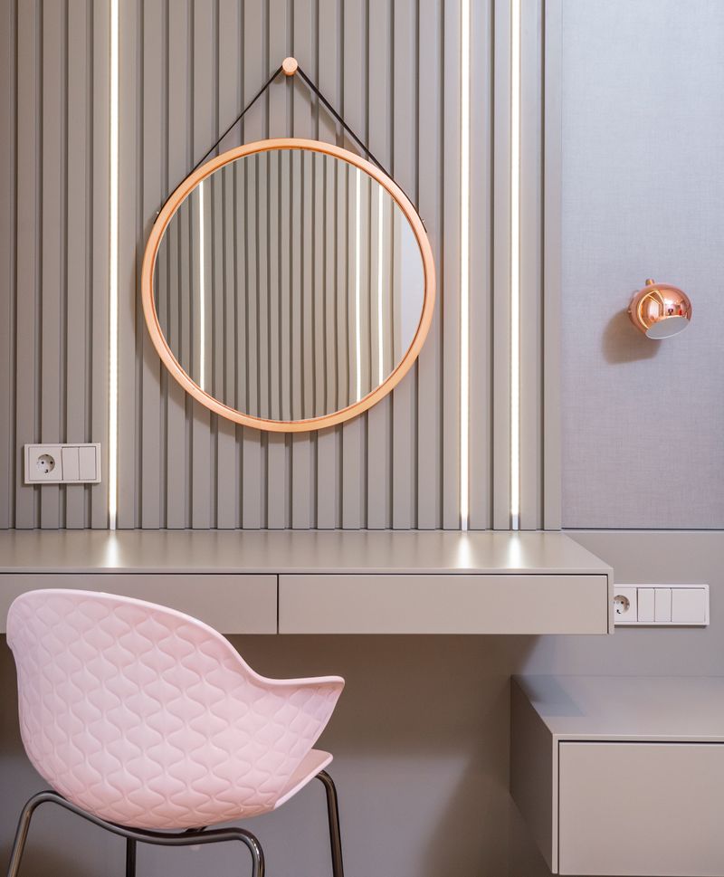 Stylish vanity table under round mirror near armchair in bedroom