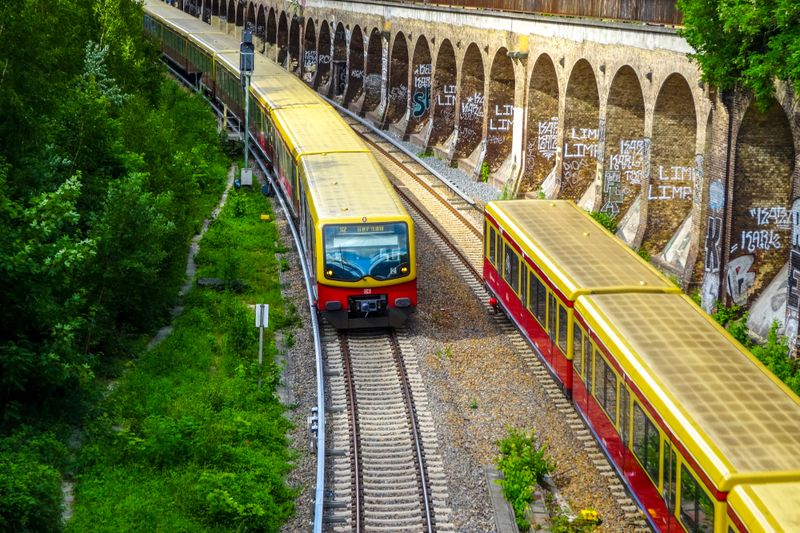 Colorful Berlin S-Bahn trains traveling on tracks beside graffiti-covered walls, capturing urban transit.