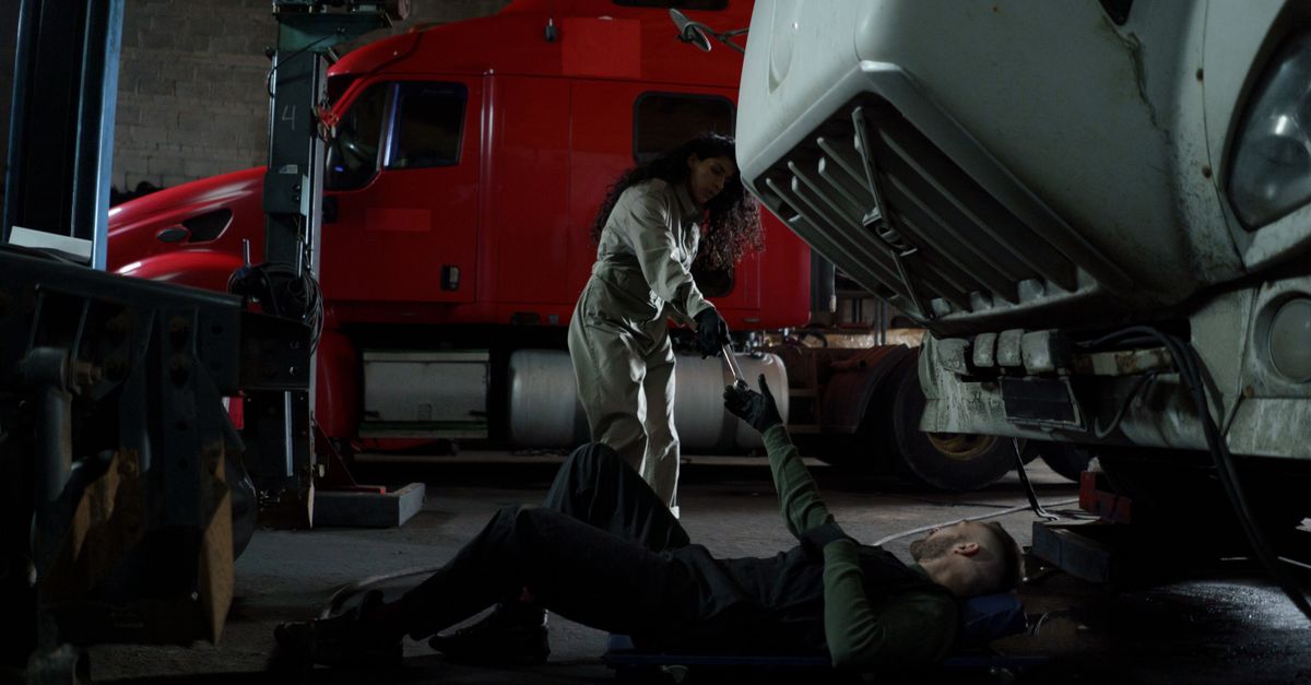 Two mechanics working together to repair a truck in a dimly lit garage setting.