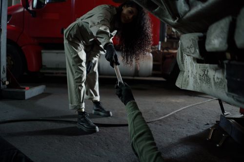 Free A mechanic handing a wrench in a dimly lit garage workshop, showing teamwork in auto repair. Stock Photo
