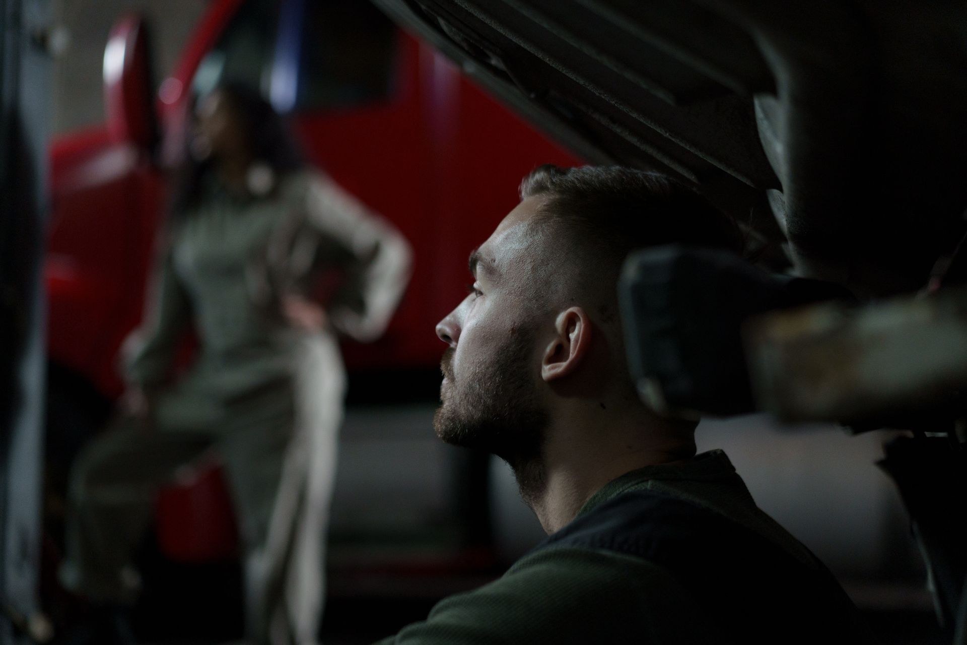 Auto mechanic focused on work in a dimly lit garage with blurred background and repair atmosphere.